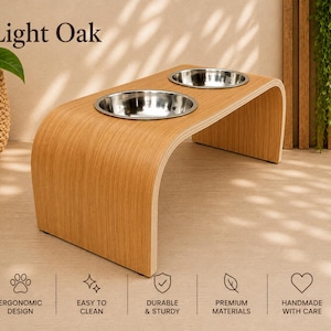 Light oak raised wooden dog bowl stand with stainless steel bowls, handmade elevated pet feeder displayed in a contemporary home, stylish feeding station for dogs and cats.