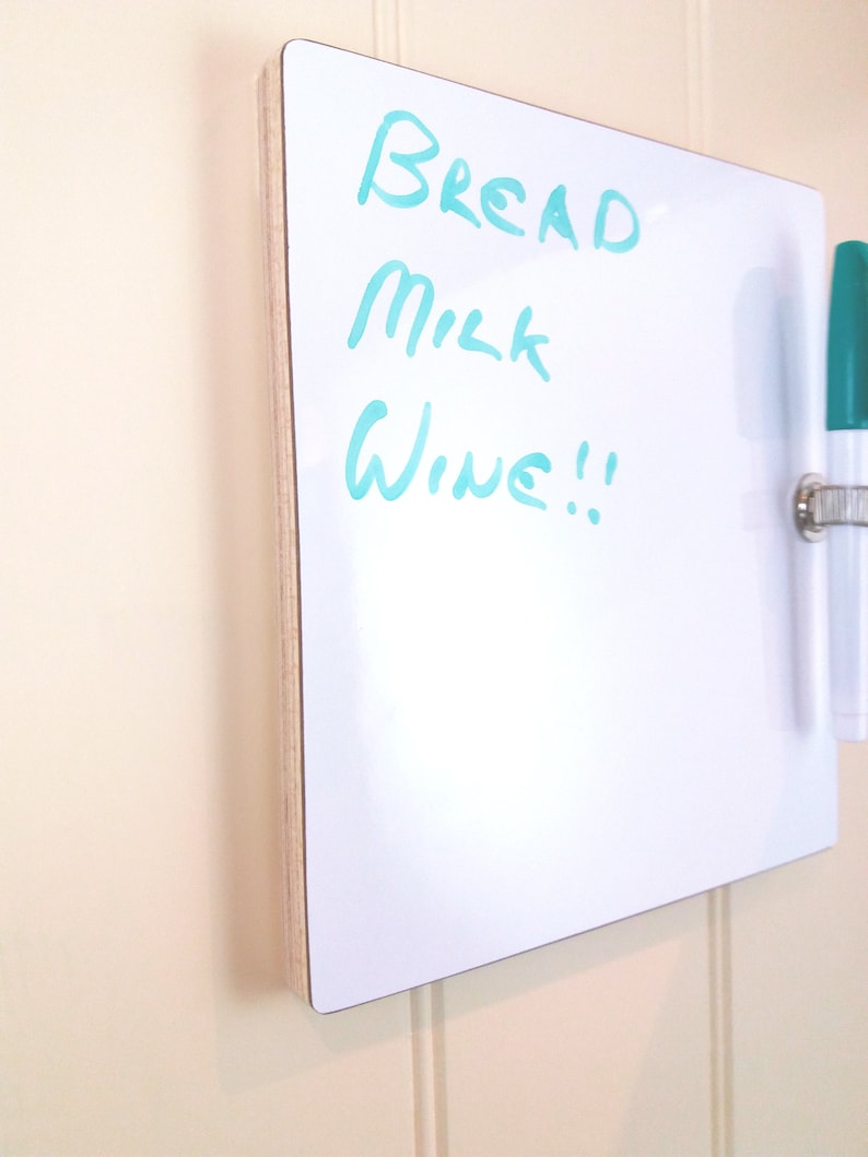 Angled view of small whiteboard / message board / fridge board attached by Velcro pads, pen and pen holder included with a natural wood trim on a white background.