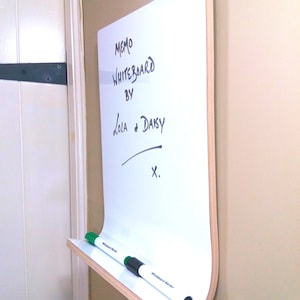 Angled view of a whiteboard with a shelf ideal for pens or keys with a natural wood trim on a wall.
