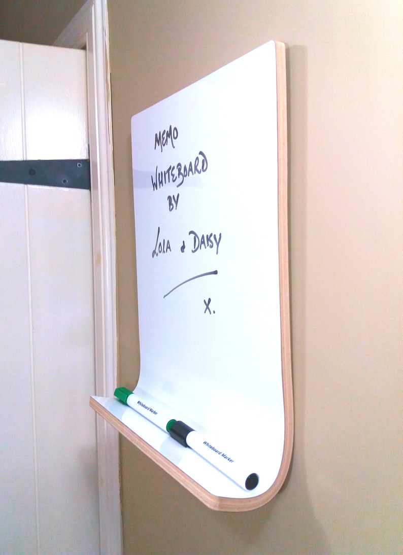 Angled view of a whiteboard with a shelf ideal for pens or keys with a natural wood trim on a wall.