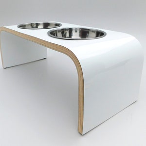 Angled view of White gloss double raised dog feeder with stainless steel bowls and natural wood edge finish.