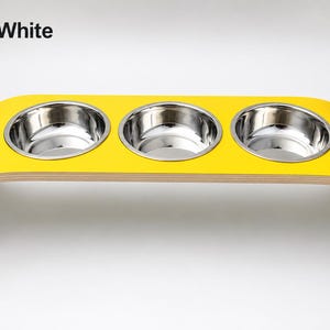 Modern yellow and white raised triple dog bowl stand with stainless steel bowls, handcrafted curved wooden pet feeder for dogs and cats.