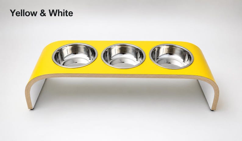 Modern yellow and white raised triple dog bowl stand with stainless steel bowls, handcrafted curved wooden pet feeder for dogs and cats.