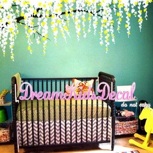 May include: A white and yellow weeping willow tree wall decal above a black crib with a chevron patterned crib skirt. The crib is in a nursery with a green wall and a yellow rocking horse.