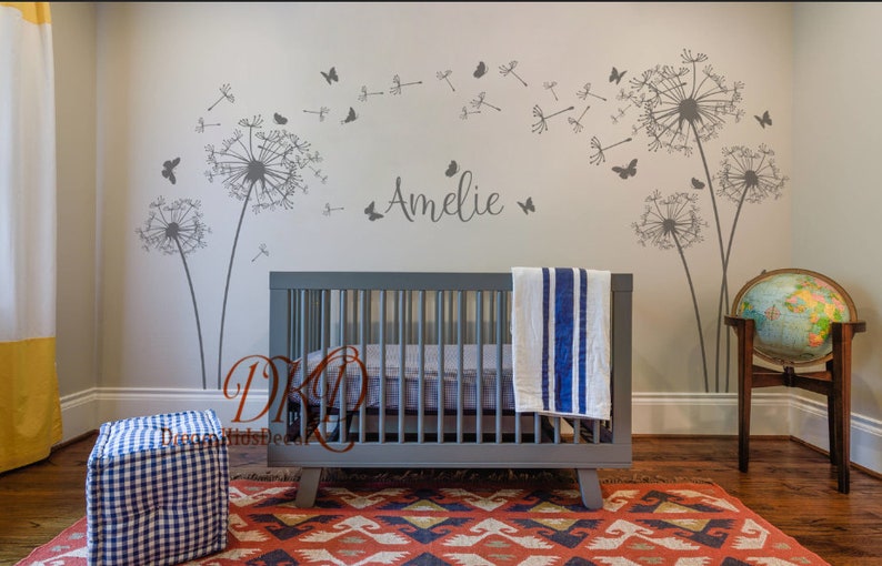 K&ouml;nnte beinhalten: Ein Kinderzimmer mit einem Babybett, einem Globus und einem Wandaufkleber mit L&ouml;wenzahnsamen, die im Wind fliegen, mit Schmetterlingen. Der Name "Amelie" steht an der Wand.