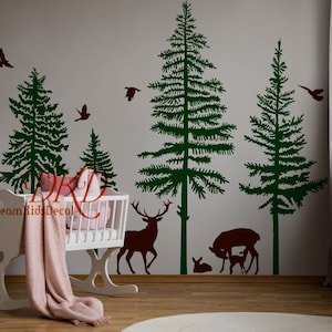 Può includere: Un set di adesivi murali con pini verde scuro e sagome di cervi marrone scuro, tra cui un cervo, una cerva e dei cerbiatti. Il design include diversi uccelli in volo tra gli alberi. Il testo DreamKidsDecal è visibile.