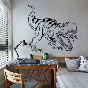 Może przedstawiać: Czarno-biała naklejka ścienna z dinozaurem przedstawiająca Tyrannosaurus Rex. Projekt znajduje się na białej ścianie. Pok&oacute;j dziecięcy ma biurko, krzesło i ł&oacute;żko. Tekst "DreamKidsDecal" znajduje się na biurku.
