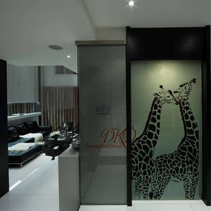 K&ouml;nnte beinhalten: Eine schwarz-wei&szlig;e Silhouette von zwei Giraffen, die sich auf einer mattierten Glasscheibe k&uuml;ssen. Die Scheibe ist schwarz gerahmt und vor einer wei&szlig;en Wand platziert.