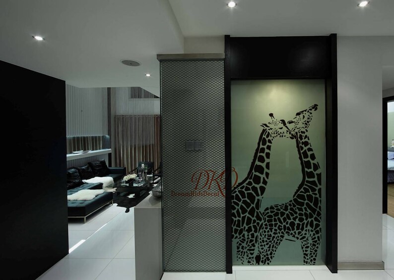 K&ouml;nnte beinhalten: Eine schwarz-wei&szlig;e Silhouette von zwei Giraffen, die sich auf einer mattierten Glasscheibe k&uuml;ssen. Die Scheibe ist schwarz gerahmt und vor einer wei&szlig;en Wand platziert.