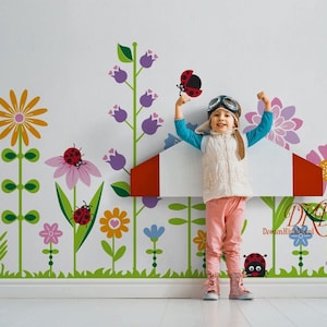 Peut inclure: Un enfant portant un gilet blanc et un pantalon rose fait semblant de piloter un avion rouge et blanc. L'enfant porte des lunettes d'aviateur et a un grand sourire. L'arrière-plan est un mur blanc avec un motif floral coloré et des coccinelles.