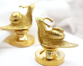 Può includere: Due sculture di lumache dorate su basi rotonde. Le lumache sono dettagliate e hanno una finitura testurizzata.