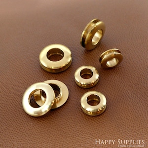 May include: Assortment of six gold-toned metal eyelets of varying sizes. The eyelets are round with a hole in the center.
