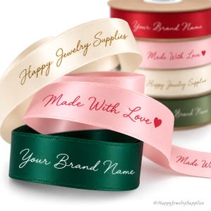 May include: A collection of satin ribbons in cream, light pink, and dark green. The cream ribbon features the text Happy Jewelry Supplies, the pink ribbon displays Made With Love with a heart icon, and the green ribbon shows Your Brand Name.