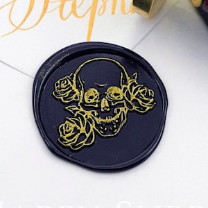 A black round wax seal on the envelope. A wax stamp above the seal.In the seal, 2 roses at the skull's left side, one connect the mouth  and another connect the head. A rose touch the skull's right eye. The skull and rose are painted in gold.