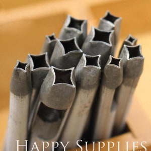May include: A set of metal punches with a diamond-shaped cutout. The punches are arranged in a pile, with the largest punch at the bottom and the smallest punch at the top. The punches are all made of a silver-colored metal.