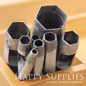 May include: A set of eight metal hexagonal hole punches in various sizes, arranged in a wooden box. The punches are used for crafting and leatherwork.