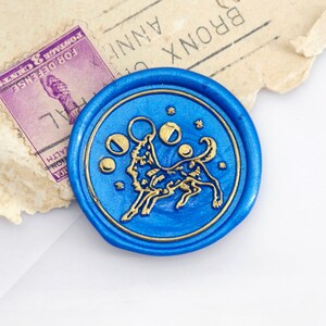 May include: A blue wax seal with a gold design of a wolf howling at the moon. The seal is circular and has a raised edge.