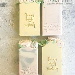 May include: Four handmade soap bars with floral embellishments. Two bars feature the text "There is beauty in simplicity" and the other two bars feature the text "Hand Made with Love".