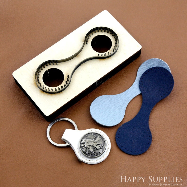 May include: A wooden leather punch tool with two round cutouts. The tool is used to create leather shapes for crafts. Two leather pieces are shown, one blue and one light blue, cut with the tool. A white leather keychain with a silver coin is also shown.