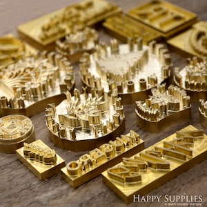 May include: A collection of brass stamps with various designs and lettering, including a leaf, a flower, the word "museum", and the word "jewelry".
