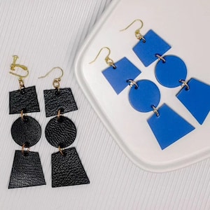 May include: Two pairs of geometric earrings. One pair is black leather with a square, circle, and triangle shape. The other pair is blue leather with a square, circle, and triangle shape.