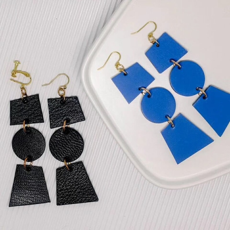 May include: Two pairs of geometric earrings. One pair is black leather with a square, circle, and triangle shape. The other pair is blue leather with a square, circle, and triangle shape.
