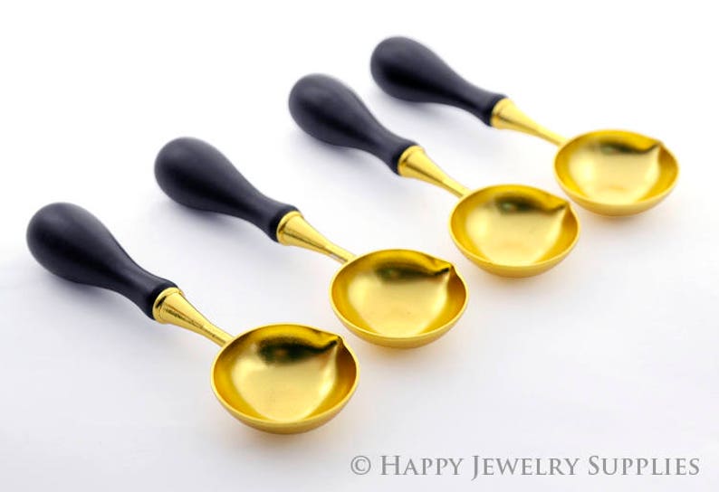 May include: Four gold-colored wax seal spoons with black wooden handles. The spoons are arranged in a row, with the handles pointing to the right.