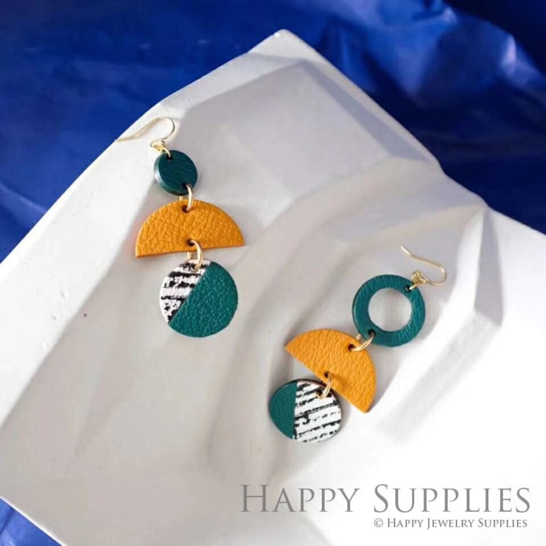 May include: A pair of dangle earrings with geometric shapes made of leather. The earrings are green, yellow, and white. The earrings are hanging from gold hooks.