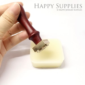 May include: A wooden handled brass stamp with a design of a series of small circles. The stamp is sitting on a white surface.