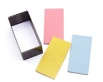 May include: Three rectangular pieces of leather in pink, yellow, and light blue. A black plastic rectangle with a cut-out rectangle in the center is also shown.