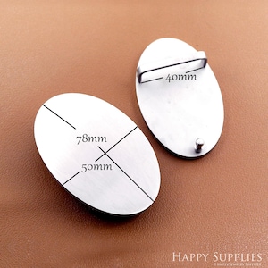 May include: Two oval-shaped, silver-colored metal belt buckles. One buckle has a 40mm bar, and the other has measurements of 78mm by 50mm. The buckles are displayed on a brown surface.