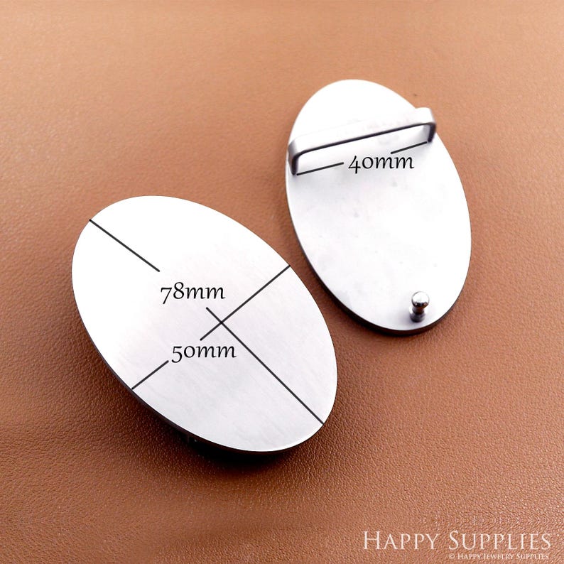 May include: Two oval-shaped, silver-colored metal belt buckles. One buckle has a 40mm bar, and the other has measurements of 78mm by 50mm. The buckles are displayed on a brown surface.