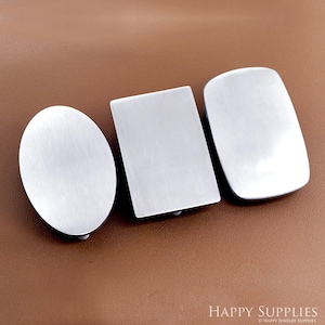 May include: Three brushed silver metal belt buckles in different shapes: an oval, a rectangle, and a rounded rectangle. The buckles are displayed on a brown surface. The Happy Supplies logo is visible in the bottom right corner.