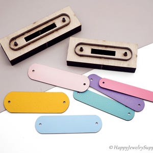 Può includere: Strumenti di taglio in legno con contorni metallici e una varietà di etichette in pelle colorate. Le etichette sono in tonalità di giallo, blu, rosa, viola e verde acqua. Ogni etichetta ha due fori preforati.