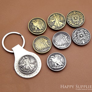 May include: A set of eight silver and gold-toned metal keychains featuring various designs, including eagles, Native American headdresses, and floral patterns. The keychains are displayed on a brown surface.