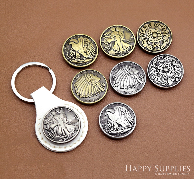 May include: A set of eight silver and gold-toned metal keychains featuring various designs, including eagles, Native American headdresses, and floral patterns. The keychains are displayed on a brown surface.