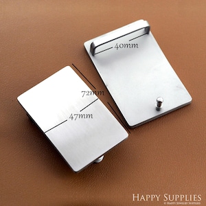May include: Two rectangular silver-colored belt buckles. One buckle has a handle and measures 40mm wide. The other buckle measures 47mm by 72mm. The buckles are displayed on a brown surface. The image includes the text "HAPPY SUPPLIES".