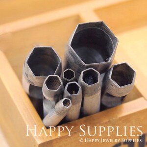 May include: A set of metal hole punches in various sizes, arranged in a wooden box. The punches are silver and have a hexagonal shape. The box is made of light brown wood and has the text "HAPPY SUPPLIES" printed on the front.