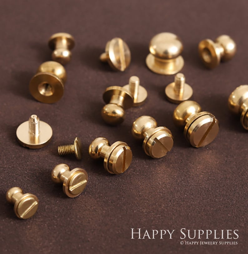 K&ouml;nnte beinhalten: Sortiment an Messing-Schraubnieten mit rundem Kopf und flachem Boden. Die Nieten sind auf einer braunen Oberfl&auml;che angeordnet. HAPPY SUPPLIES &copy; HAPPY JEWELRY SUPPLIES.