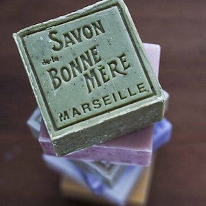 May include: A stack of green, purple, blue, and yellow soap bars. The top bar is green and has the text "Savon de la Bonne Mere Marseille" printed on it.
