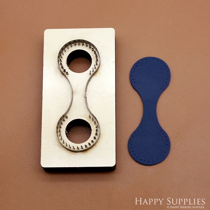 May include: A wooden leather craft punch tool with two round cutouts. The tool is used to create a leather loop with two circles. A blue leather loop is shown next to the tool.