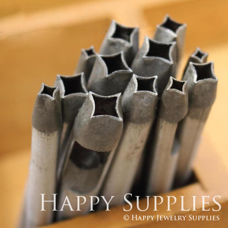May include: A set of metal punches with a diamond-shaped cutout. The punches are arranged in a pile, with the largest punch at the bottom and the smallest punch at the top. The punches are all made of a silver-colored metal.