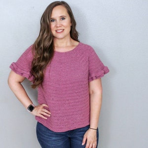 May include: A mauve crochet top with short sleeves and ruffled edges. The top has a round neckline and is made with a textured stitch.