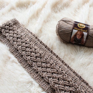 以下が含まれることがあります： ハートランドの糸で編まれた、ケーブル編みの模様の入った茶色のクロシェのストールです。