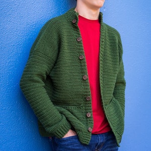 May include: A green crocheted cardigan with wooden buttons, worn over a red t-shirt and blue jeans.