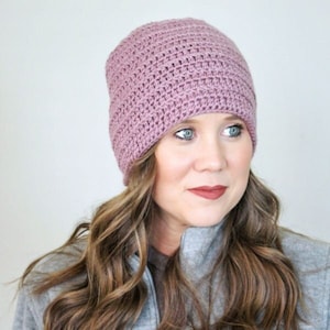 May include: A woman wearing a mauve crocheted beanie hat. The hat is made with a simple stitch pattern and has a slouchy fit.