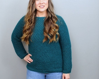 May include: A teal blue knitted jumper with a loose fit and long sleeves.