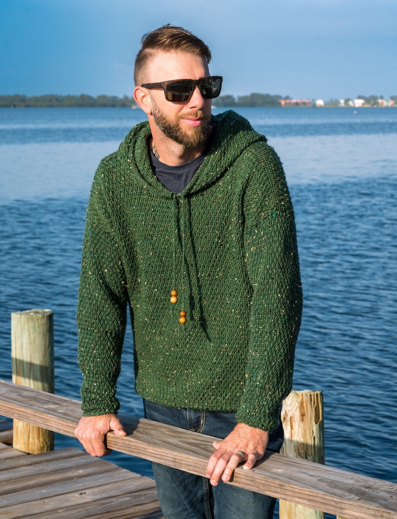 May include: A green hooded sweater with a speckled texture. The sweater has a drawstring hood and wooden beads on the drawstring.