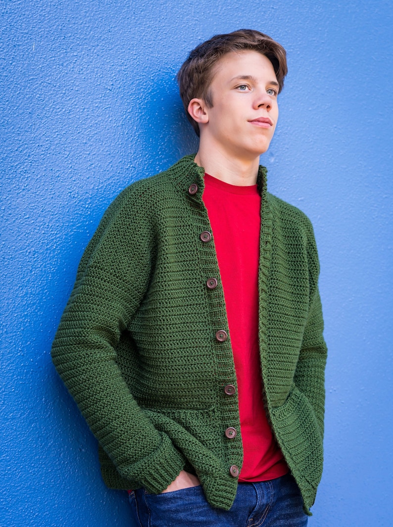 May include: A green crocheted cardigan with wooden buttons, worn over a red t-shirt and blue jeans.