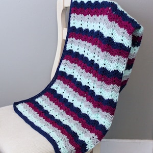 May include: A crocheted baby blanket with a wavy striped pattern in shades of teal, gray, and burgundy.